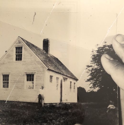 A hand holding a sepia print of a white farmhouse