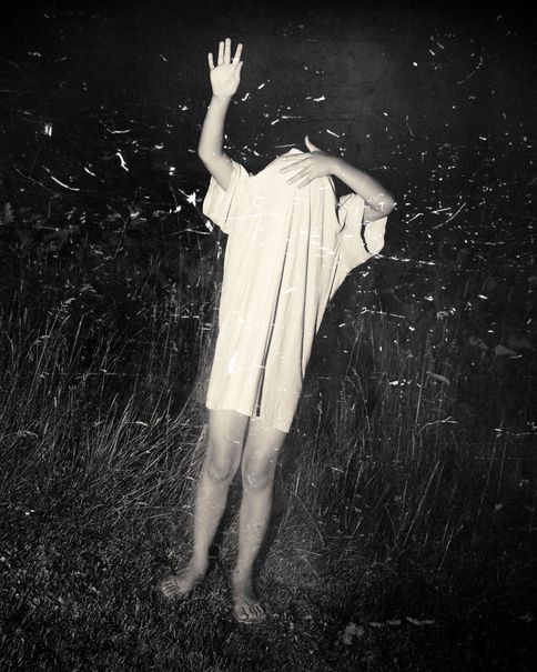 A figure with a raised arm, face covered, at night