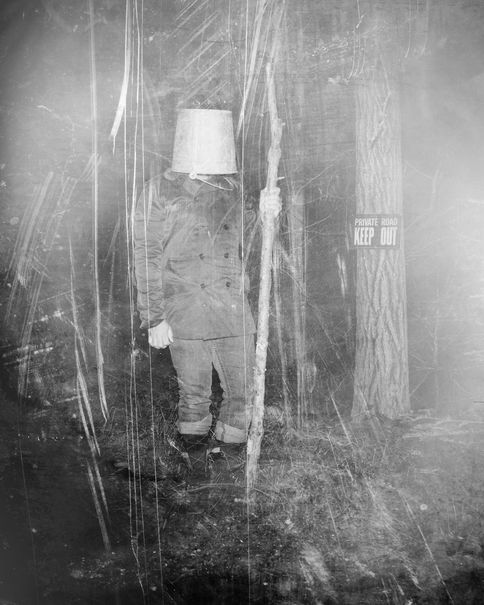 A figure with a bucket over its head among trees